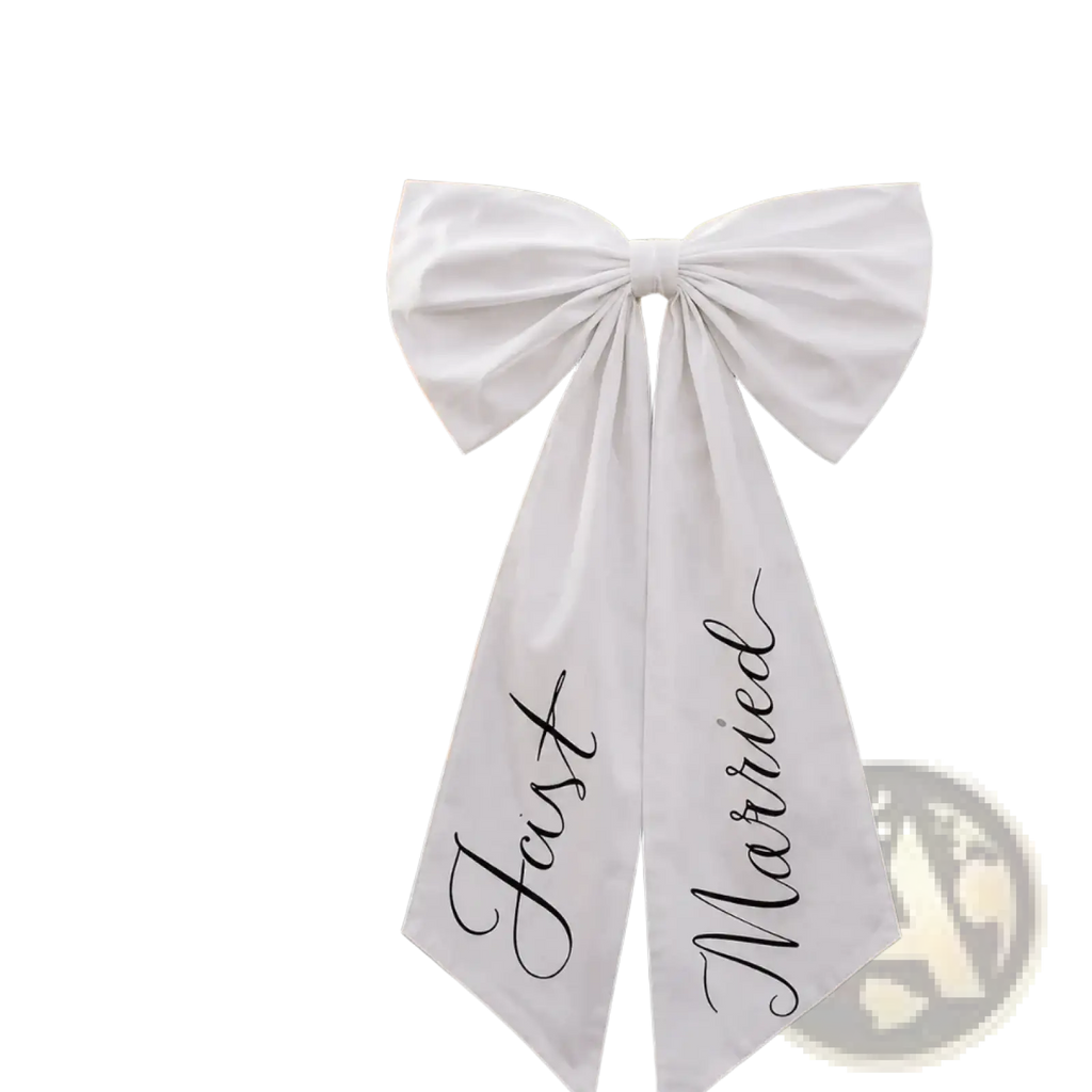 A white satin wedding car bow with just married scripted in black cursive tied to the front of a luxury car