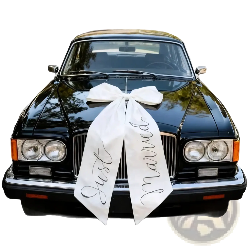 White satin wedding car bow with just married scripted in black cursive tied on a glossy black classic car