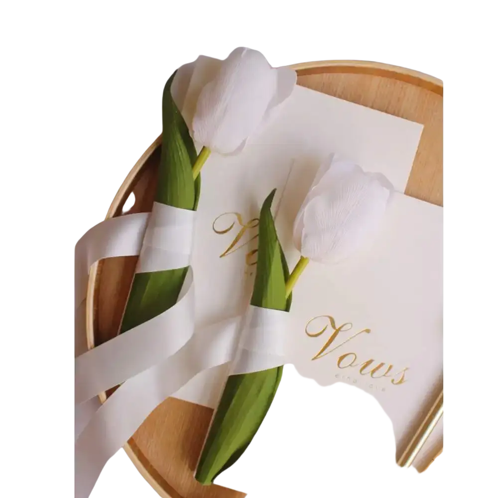 White paper tulips with green stems wrapped in white ribbon in wedding vow books set with gold keys and ribbons