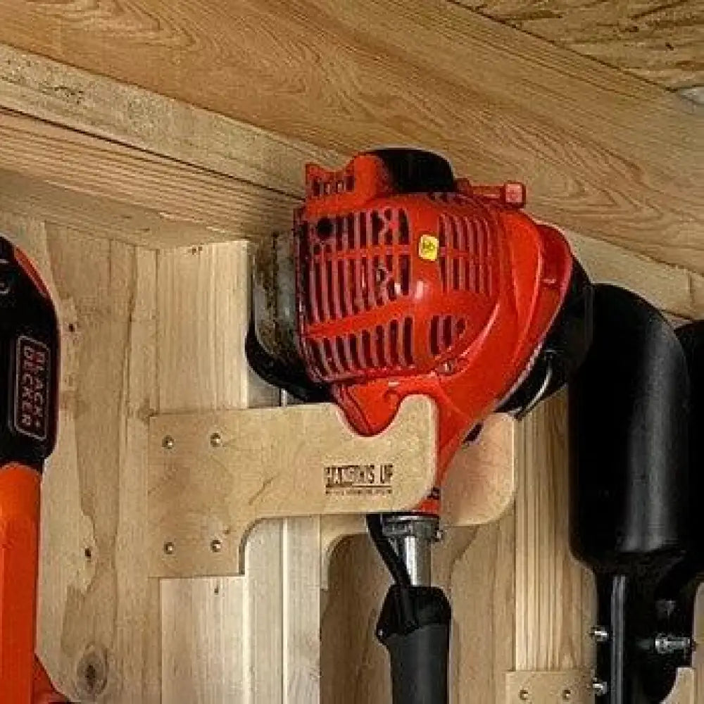 Red and black gas-powered weed wacker mounted on a wooden stud mounted wall rack for string trimmers and tools