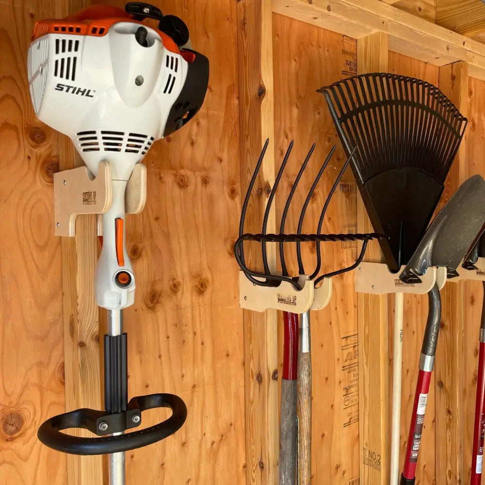 White and orange stihl gas-powered hedge trimmer mounted on a wooden stud mounted wall rack for string trimmers and tools