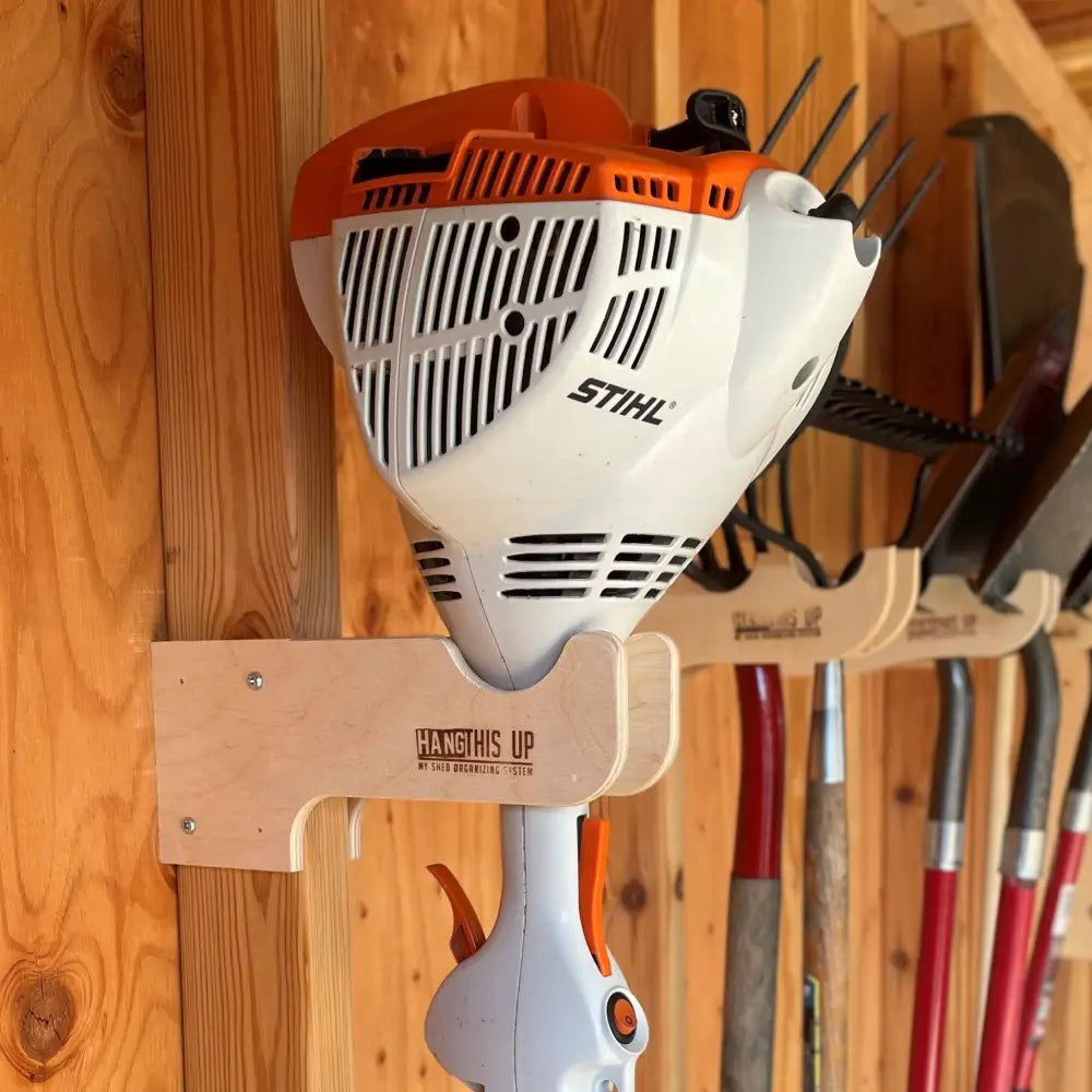 White and orange stihl hedge trimmer mounted on stud mounted wooden wall rack for string trimmers and tools