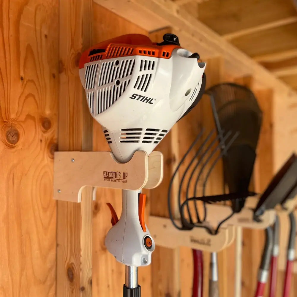 White and orange stihl string trimmer mounted on a wooden stud mounted wall rack for string trimmers and tools