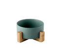A minimalist matte teal ceramic bowl supported by two light wood l-shaped stands in a product set