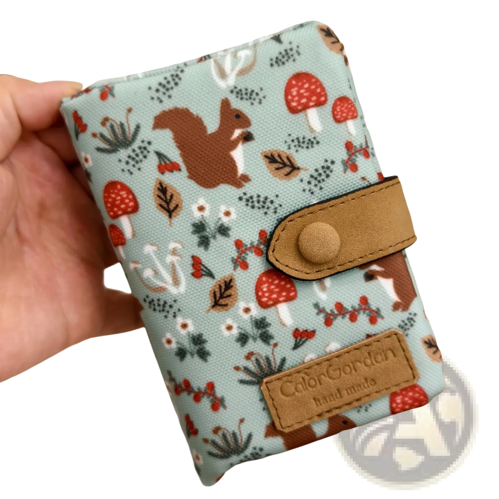 A light blue canvas tri fold multi card wallet with a whimsical forest pattern and tan leather accents