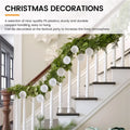 White shatterproof Christmas baubles with textured surface hanging on a green garland over a staircase railing