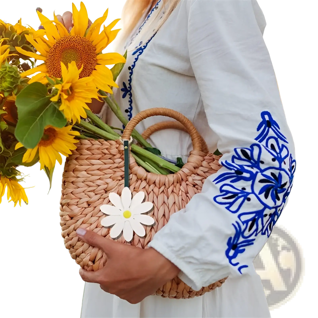 Beige woven straw handbag with natural wood handles featuring a white daisy leather bag charm keychain pendant