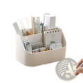 White plastic desk organizer and makeup brush holder with multiple compartments holding pens scissors and stationery items
