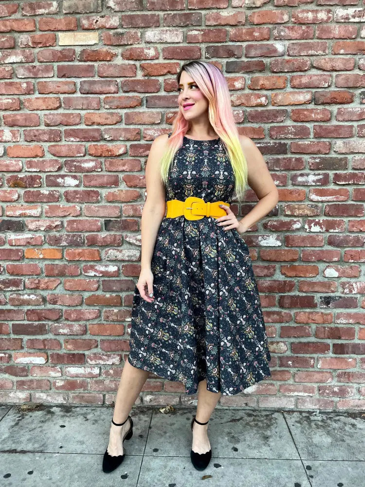 Black floral print midi dress with fitted bodice and flared skirt accented by a bold yellow belt by White Rabbit