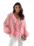 A soft pink sheer blouse with layered ruffles at the neckline and puff sleeves in a white ruffled v neck style