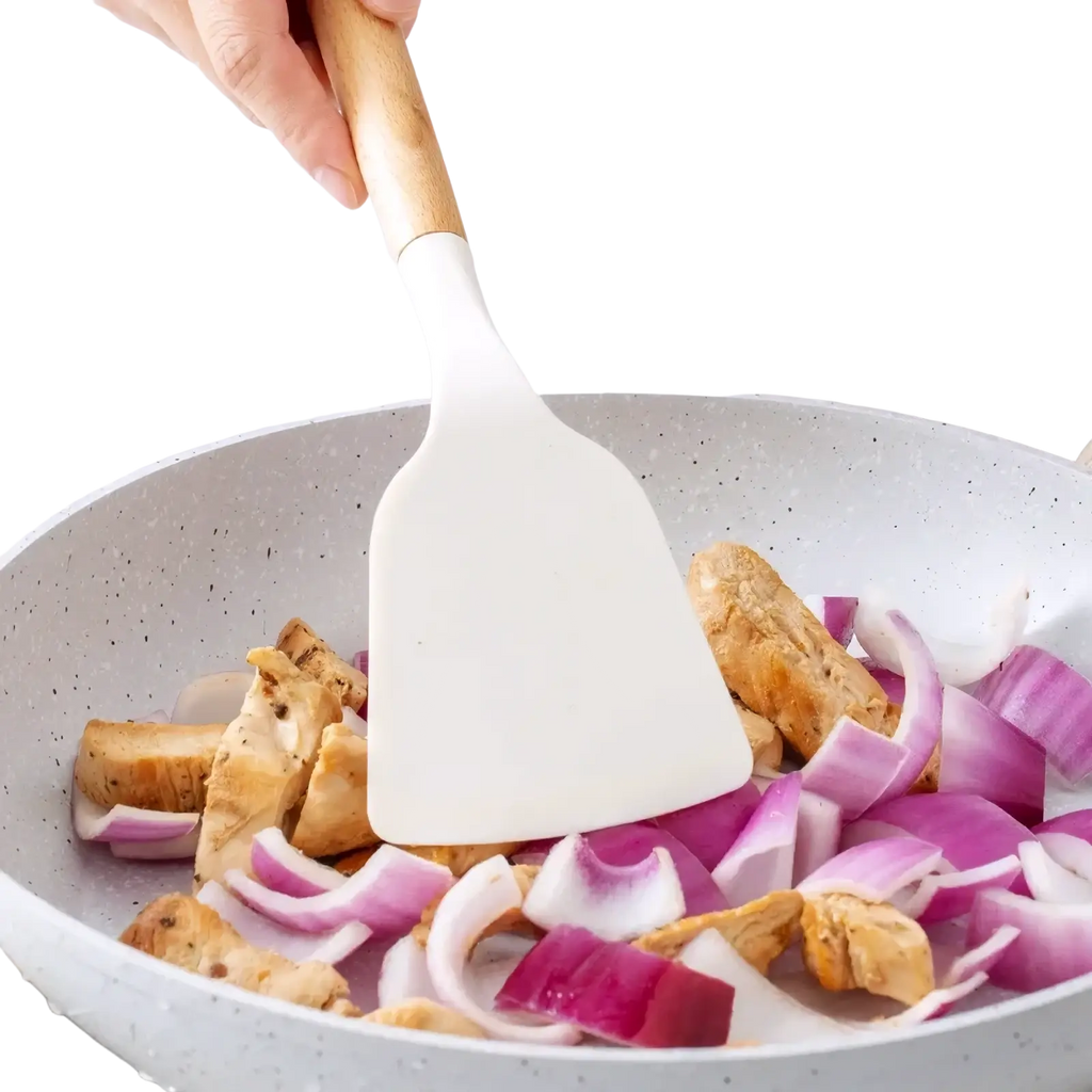 White silicone kitchen spatula with wooden handle stirring chicken and red onions in speckled gray pan