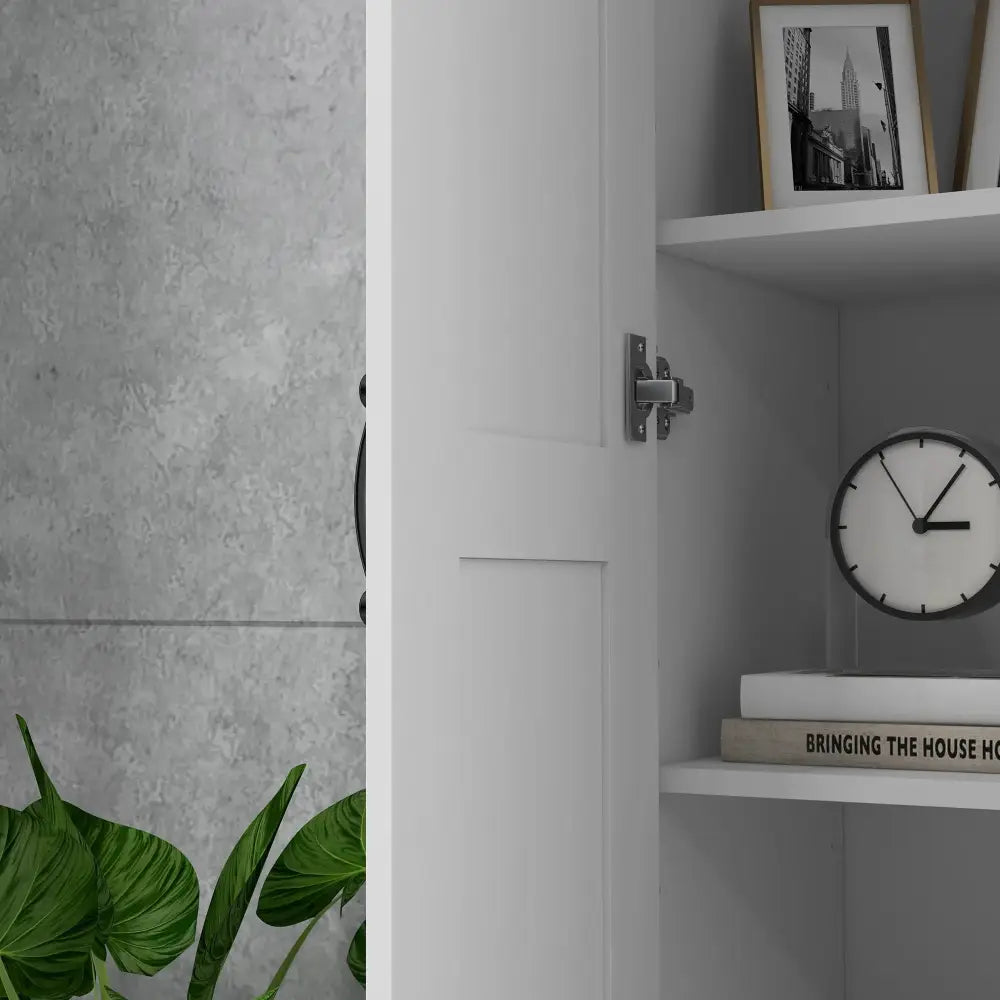 Modern tall white kitchen pantry cabinet with adjustable shelves and a partially open door revealing books and a clock