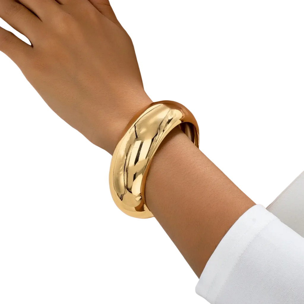 A sleek wide gold-tone bangle bracelet for women with a smooth rounded design worn on a wrist