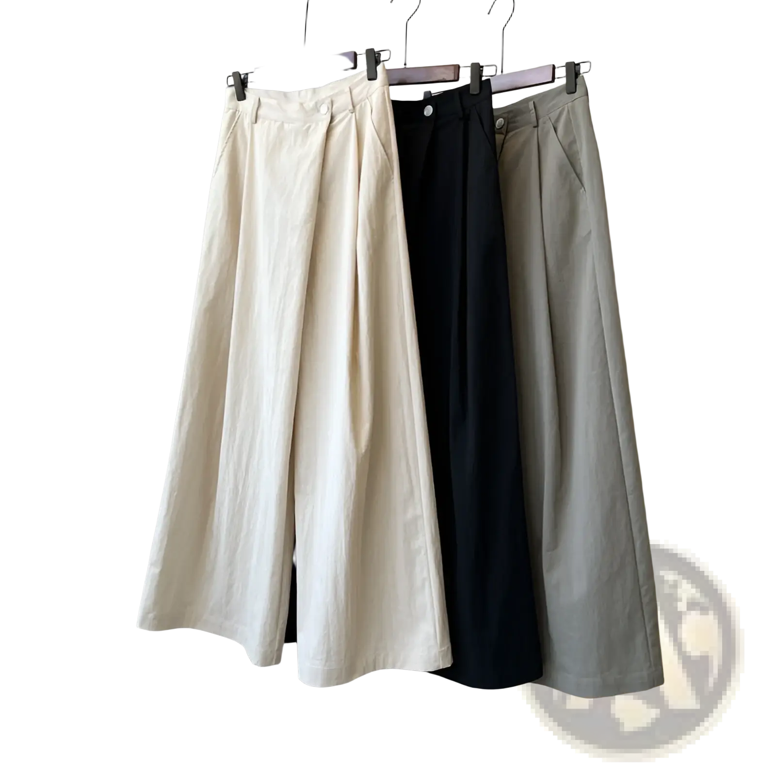 Three pairs of wide leg high waisted casual trousers in cream black and beige hanging on wooden hangers