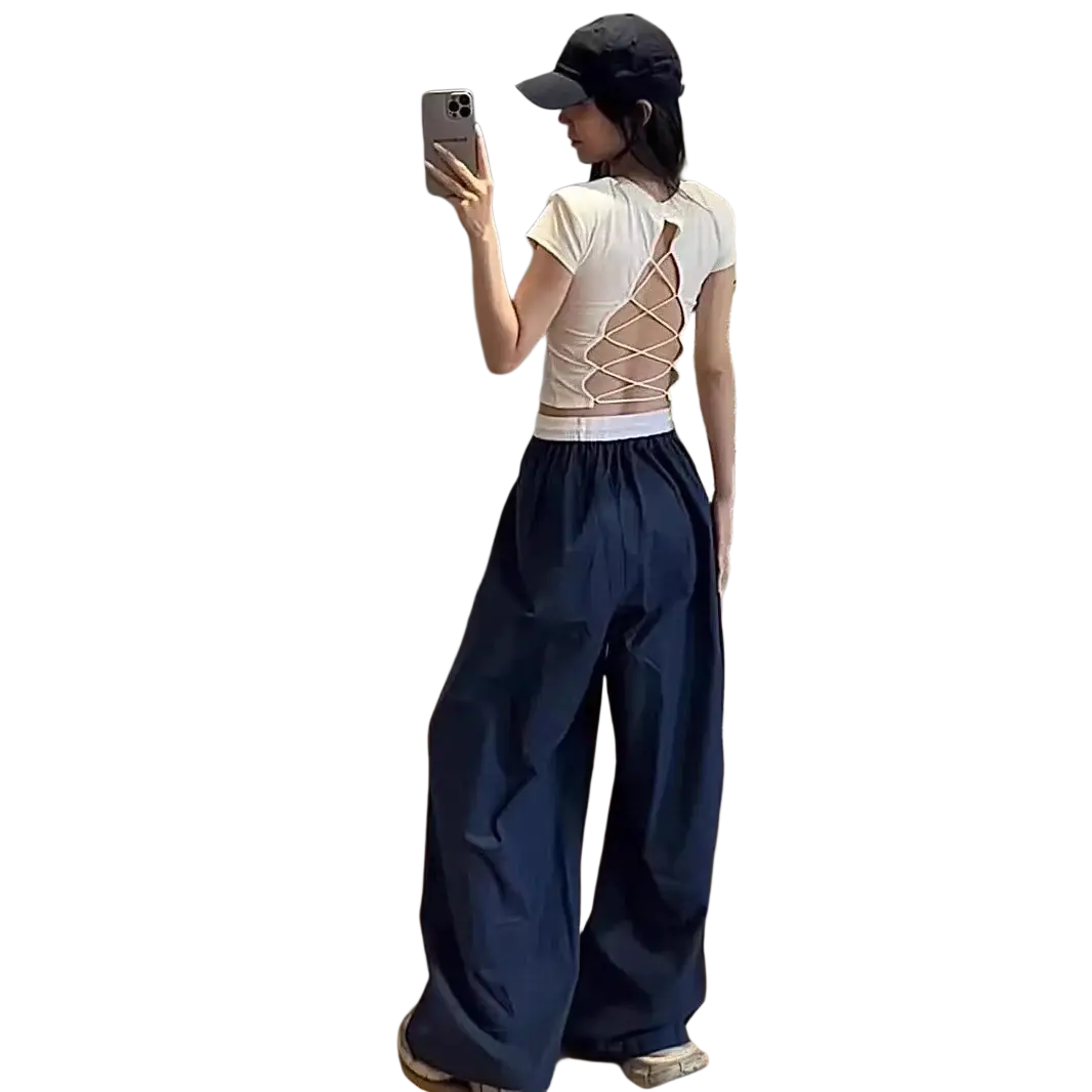 Back view of a white short-sleeved crop top with a crisscross laceback design paired with wide leg sweatpants for women