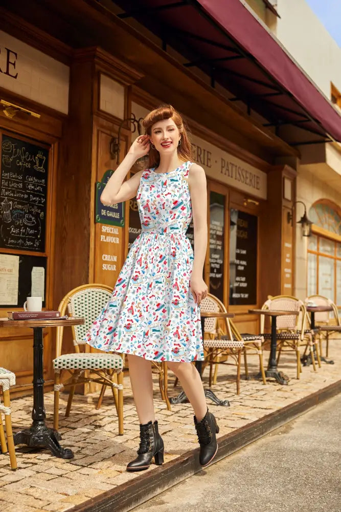 A woman wears a sleeveless knee-length cotton winter cheer vintage 1950s dress with colorful food print on light blue background