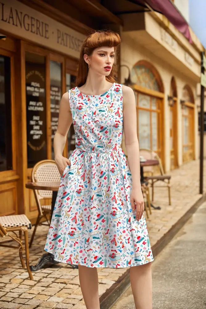 A woman wears a sleeveless knee-length winter cheer vintage 1950s cotton Christmas dress with colorful kitchen utensils