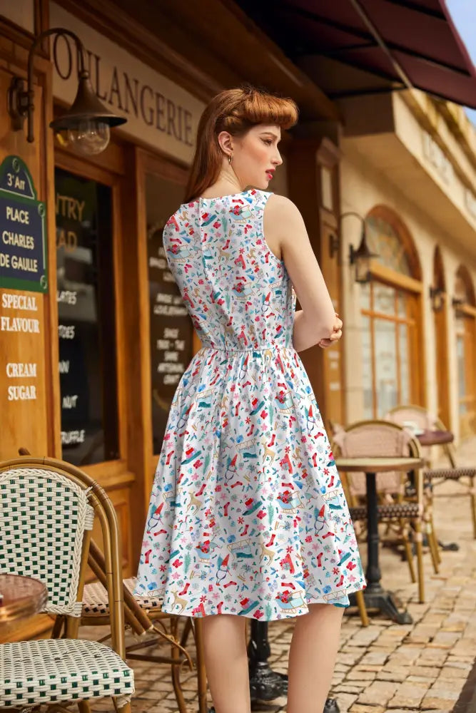 A woman wears a sleeveless winter cheer vintage 1950s cotton Christmas dress with colorful vintage-style illustrations