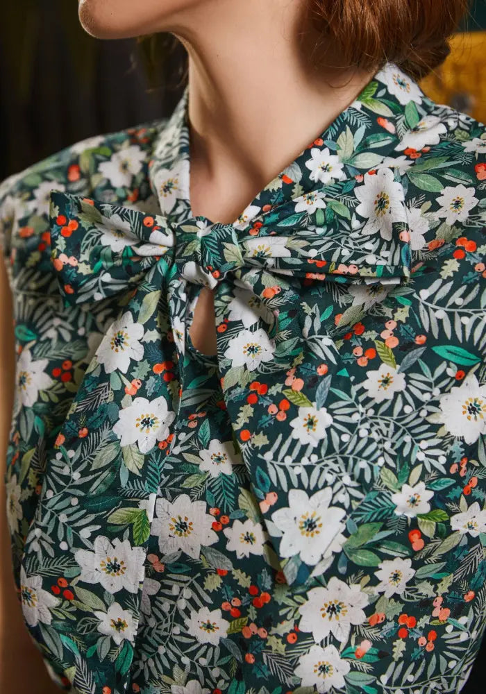 A dark green sleeveless cotton blouse with white and orange berry print and a large tied bow at the neckline