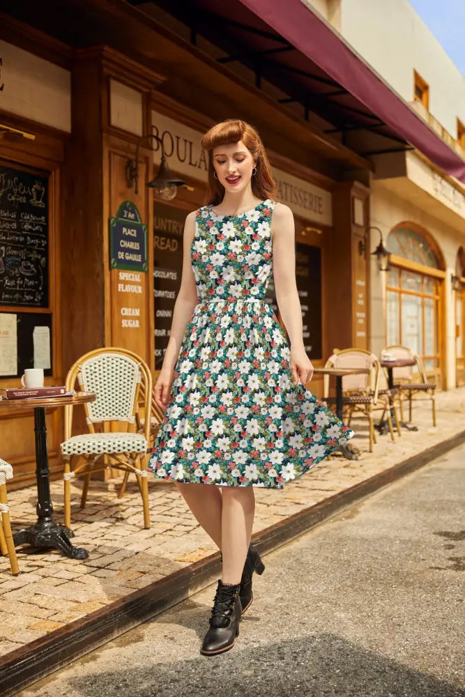 A woman walking down a cobblestone street wearing a vintage-style green floral print sleeveless cotton midi dress with pockets