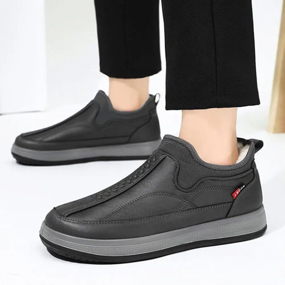 Men’s black fleece lined slip on winter snow boots with padded collar and gray rubber sole shown from back side