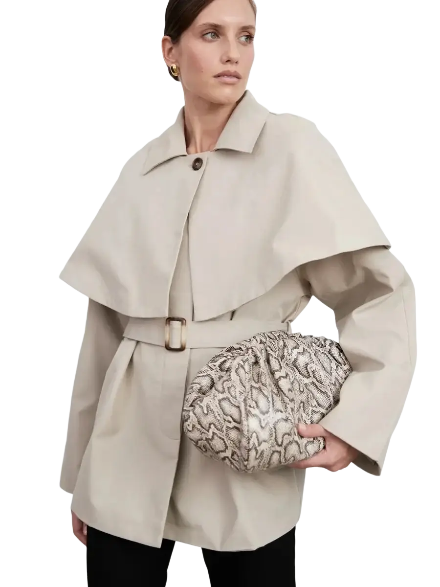 A cream and black textured snake-print clutch with a gathered puffy design complementing a women belted trench coat with cape overlay