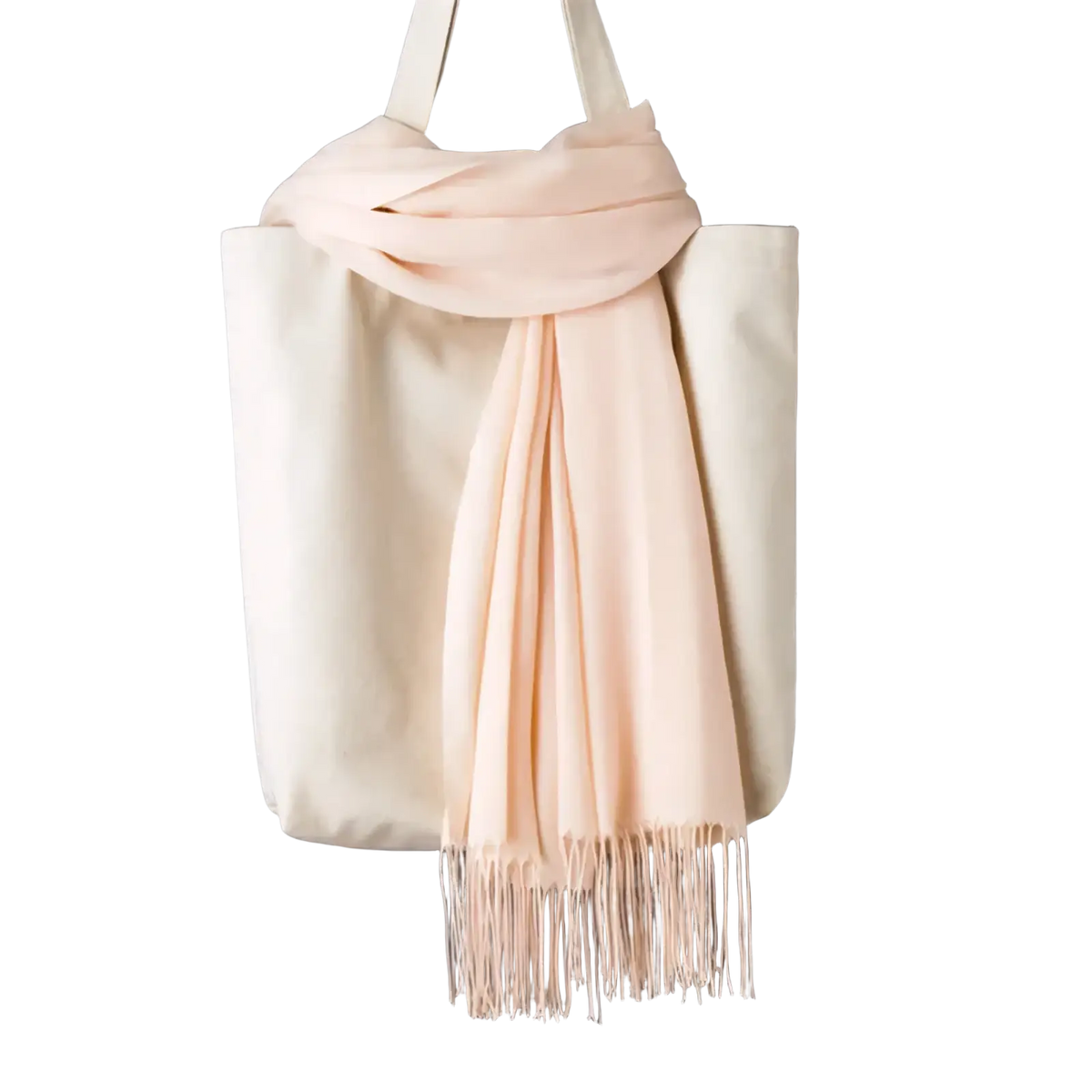 A soft blush pink cashmere feel winter scarf shawl with delicate fringe draped over a cream tote bag
