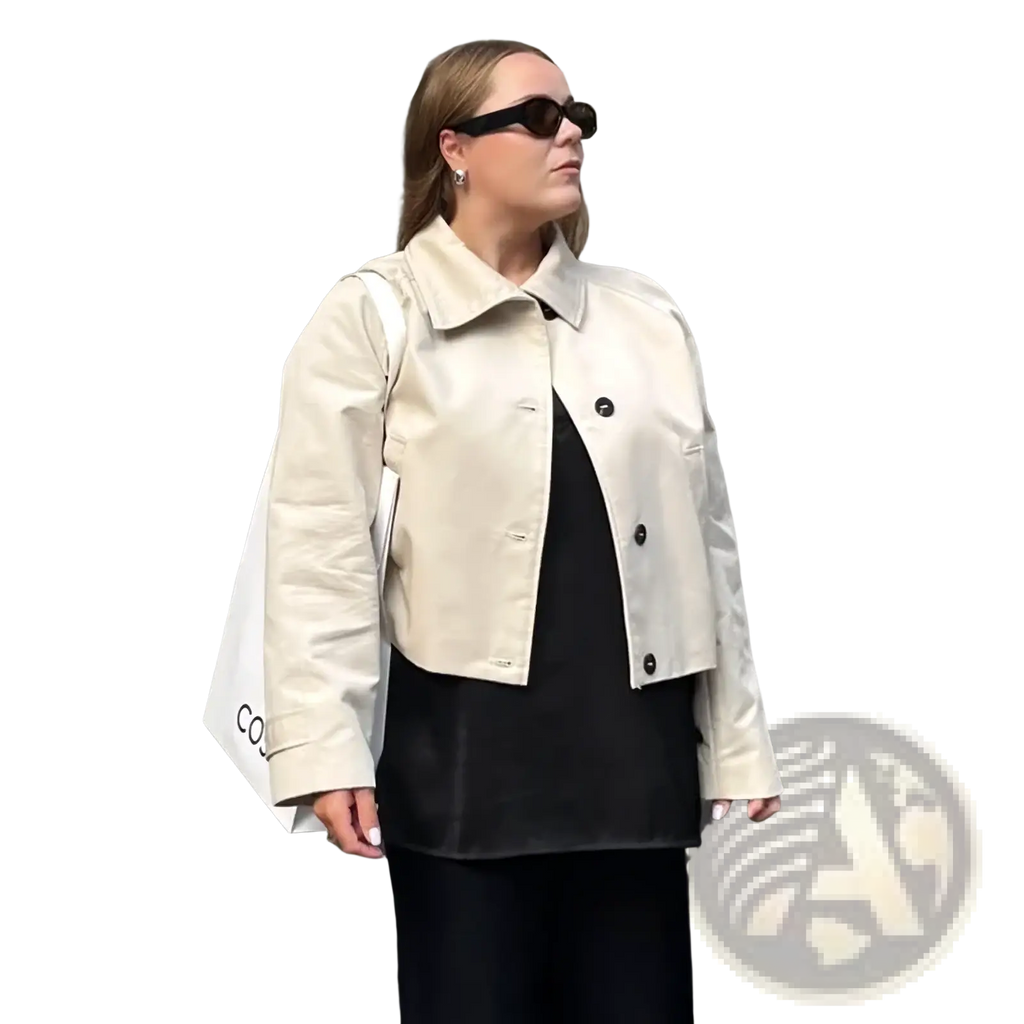 Beige cropped trench coat for women featuring black buttons and a structured collar in a short windbreaker style