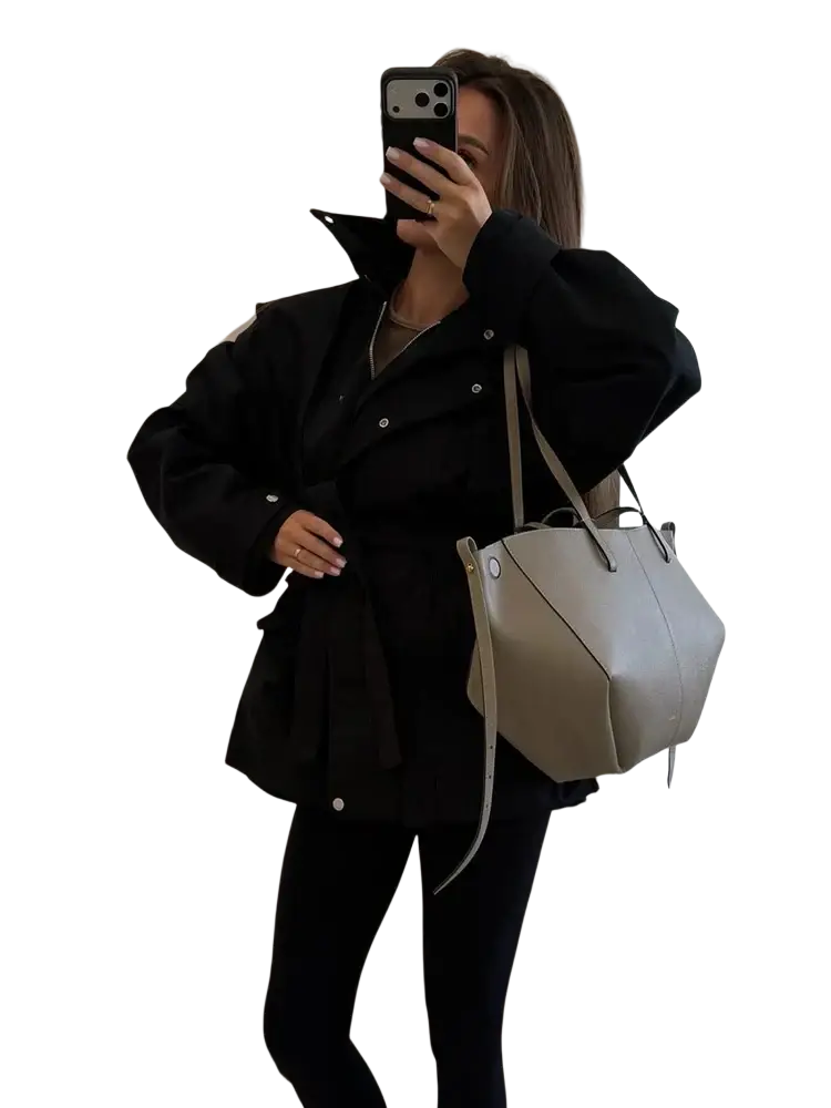 Beige leather tote bag with structured hexagonal shape and slender shoulder strap paired with women’s short beige trench coat belted utility jacket