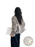 A woman wears a light gray belted short utility trench jacket with long sleeves and buttoned cuffs