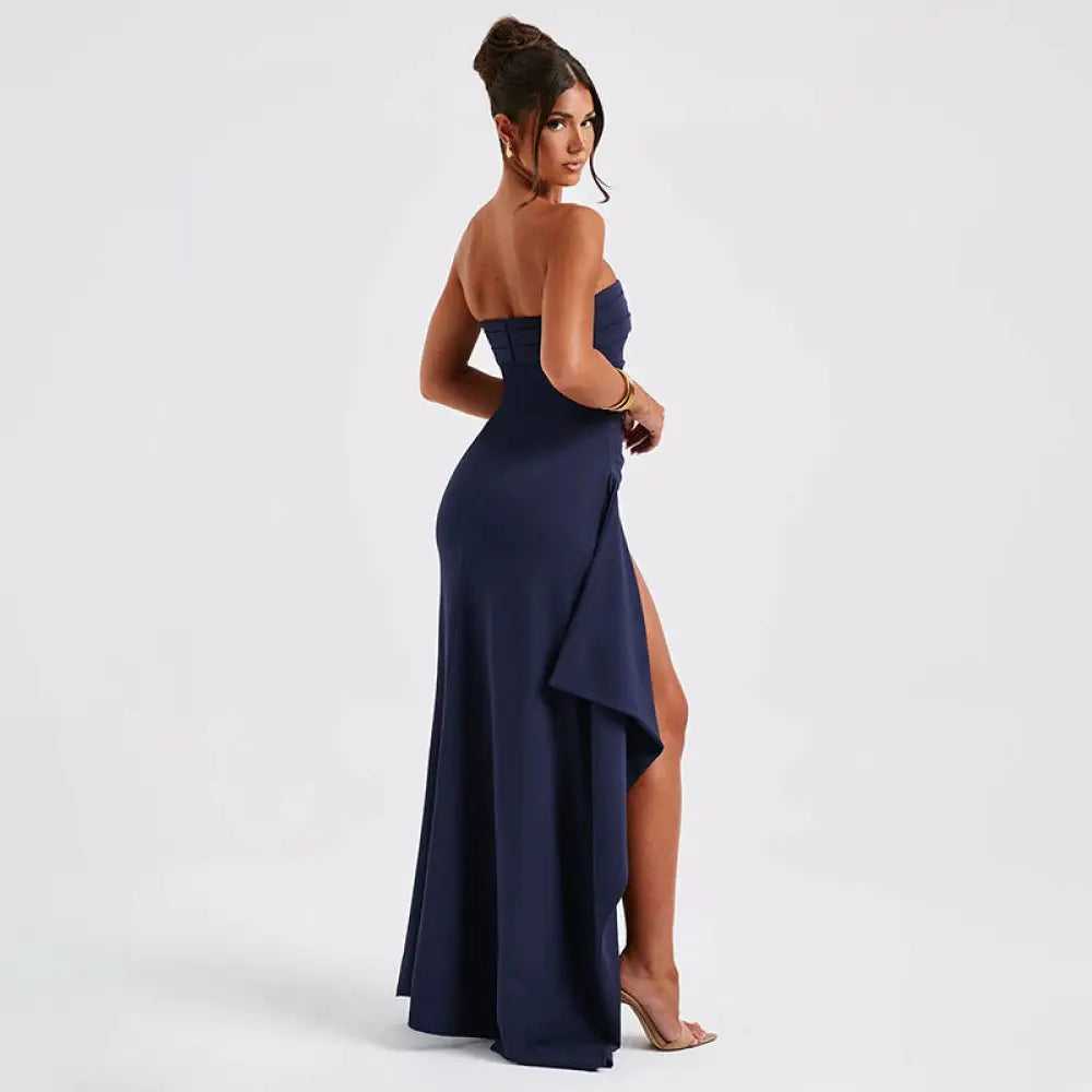 A sleek navy blue strapless pleated maxi gown with ruched bodice and high slit featuring flowing fabric