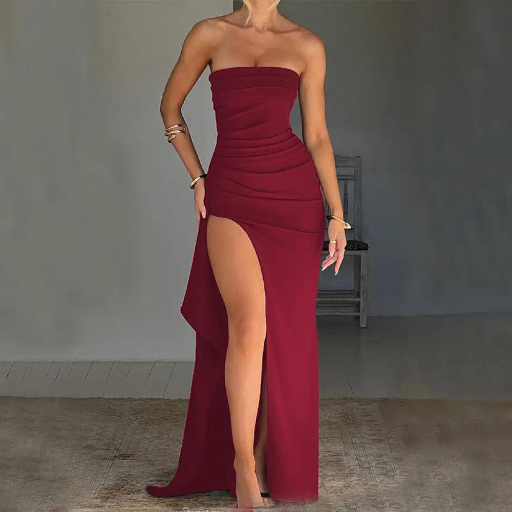 Strapless pleated maxi gown in burgundy with a ruched bodice and high slit, designed for elegant evening wear