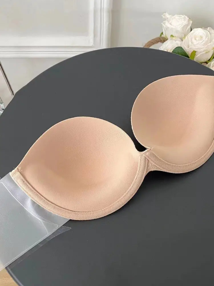 Beige adhesive strapless push up bra with smooth seamless design and transparent tape backing shown from the back side