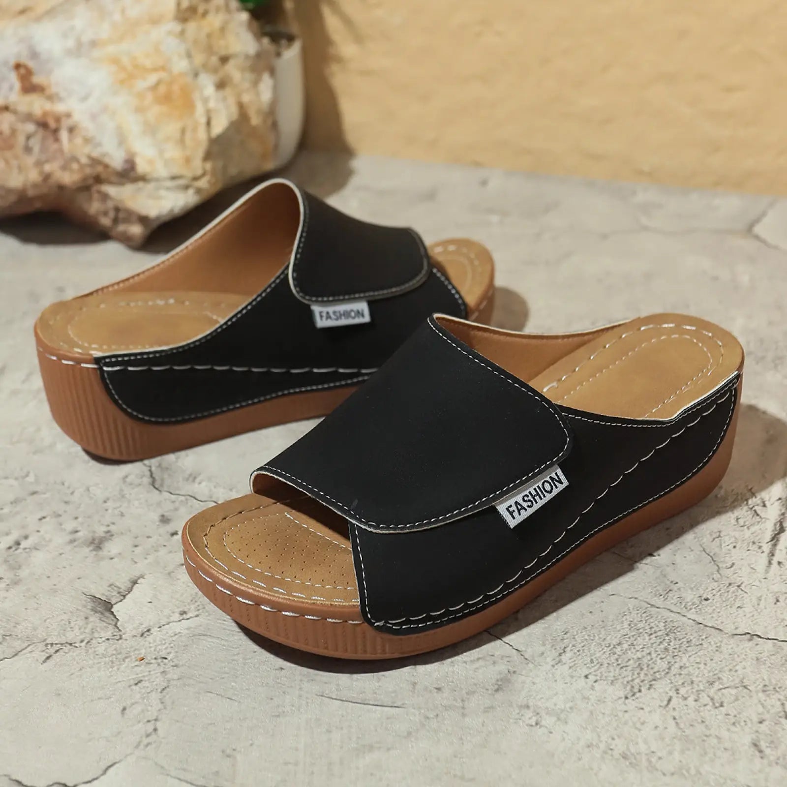 Sandales d’été à plateforme compensée à bride glissante pour femmes de type daim noir, avec une semelle en caoutchouc beige, des coutures blanches et une petite étiquette de mode sur la bride.
