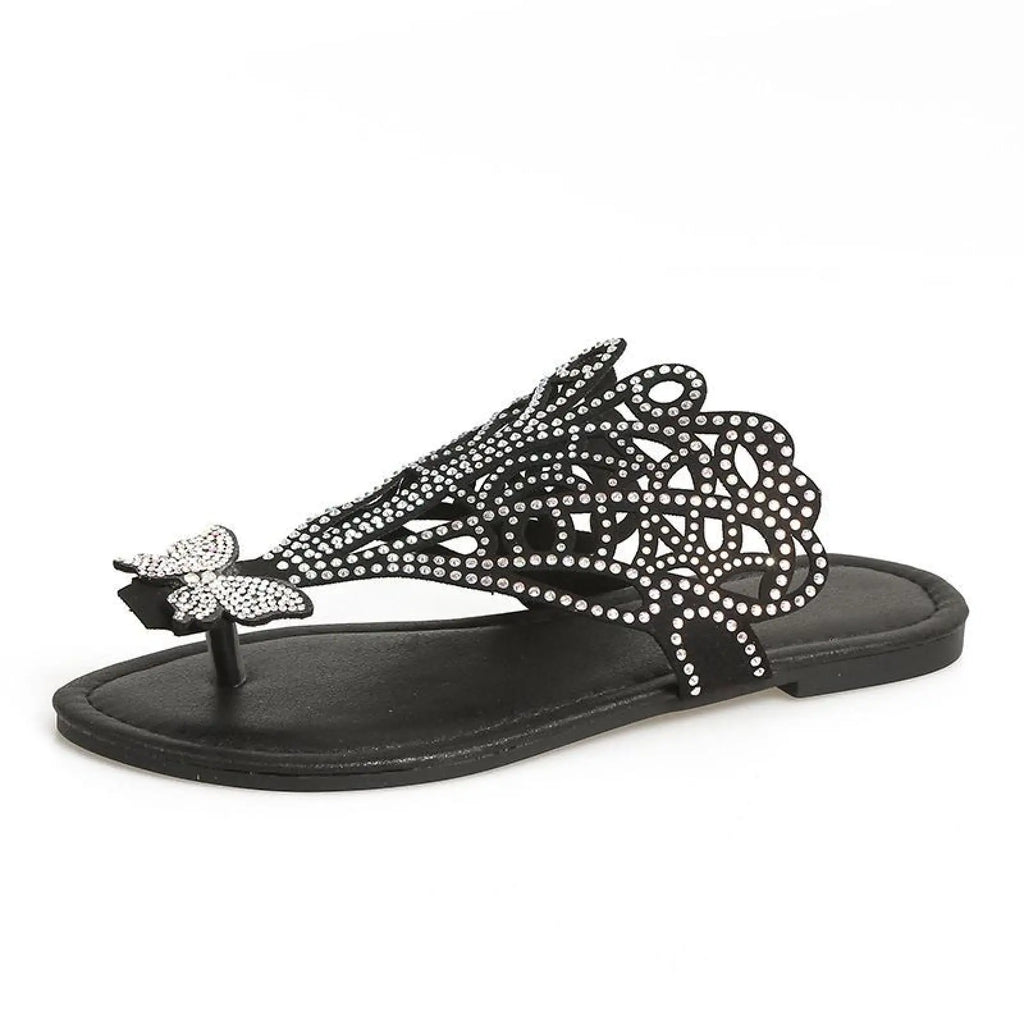 Black women’s rhinestone hollow flat slip on sandal with intricate cutout design and decorative butterfly accent on toe strap