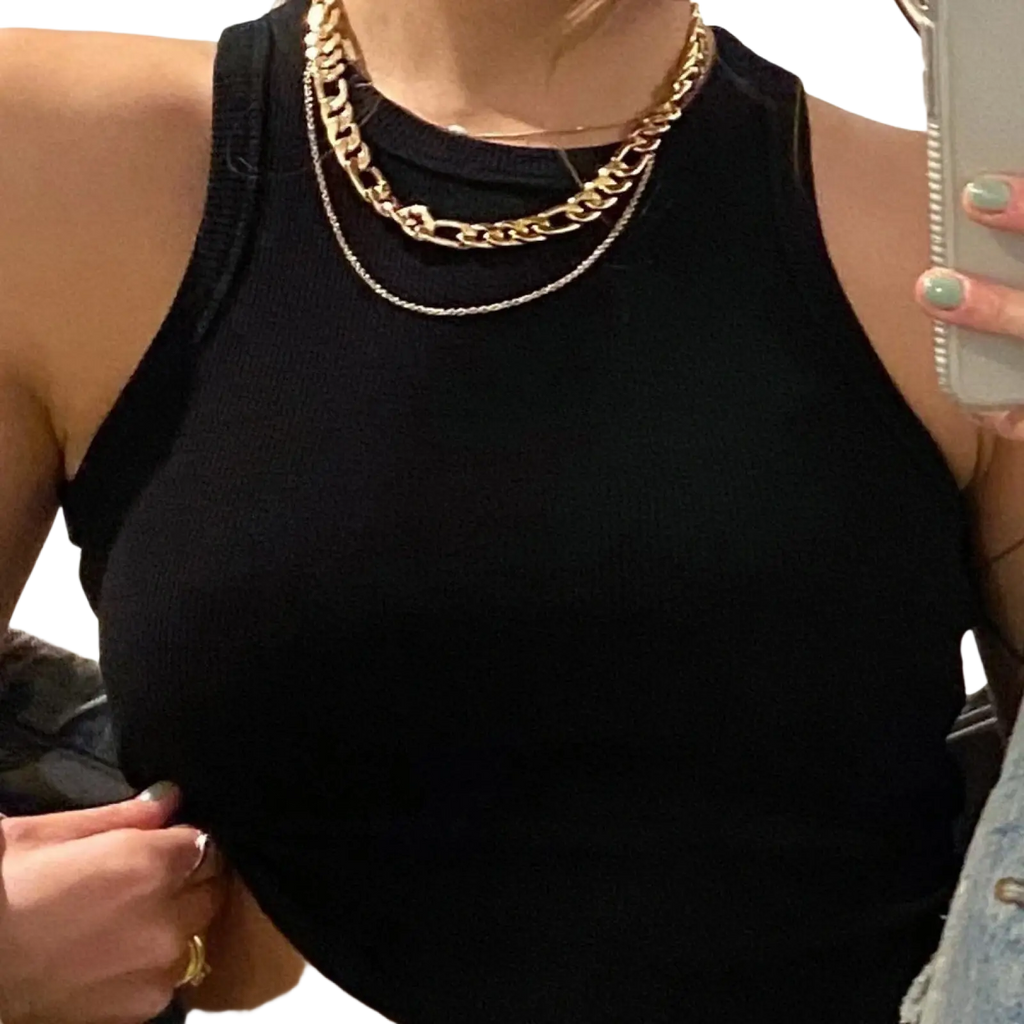 Woman wearing gold and silver layered chain necklaces over a black ribbed sleeveless slim fit crop top