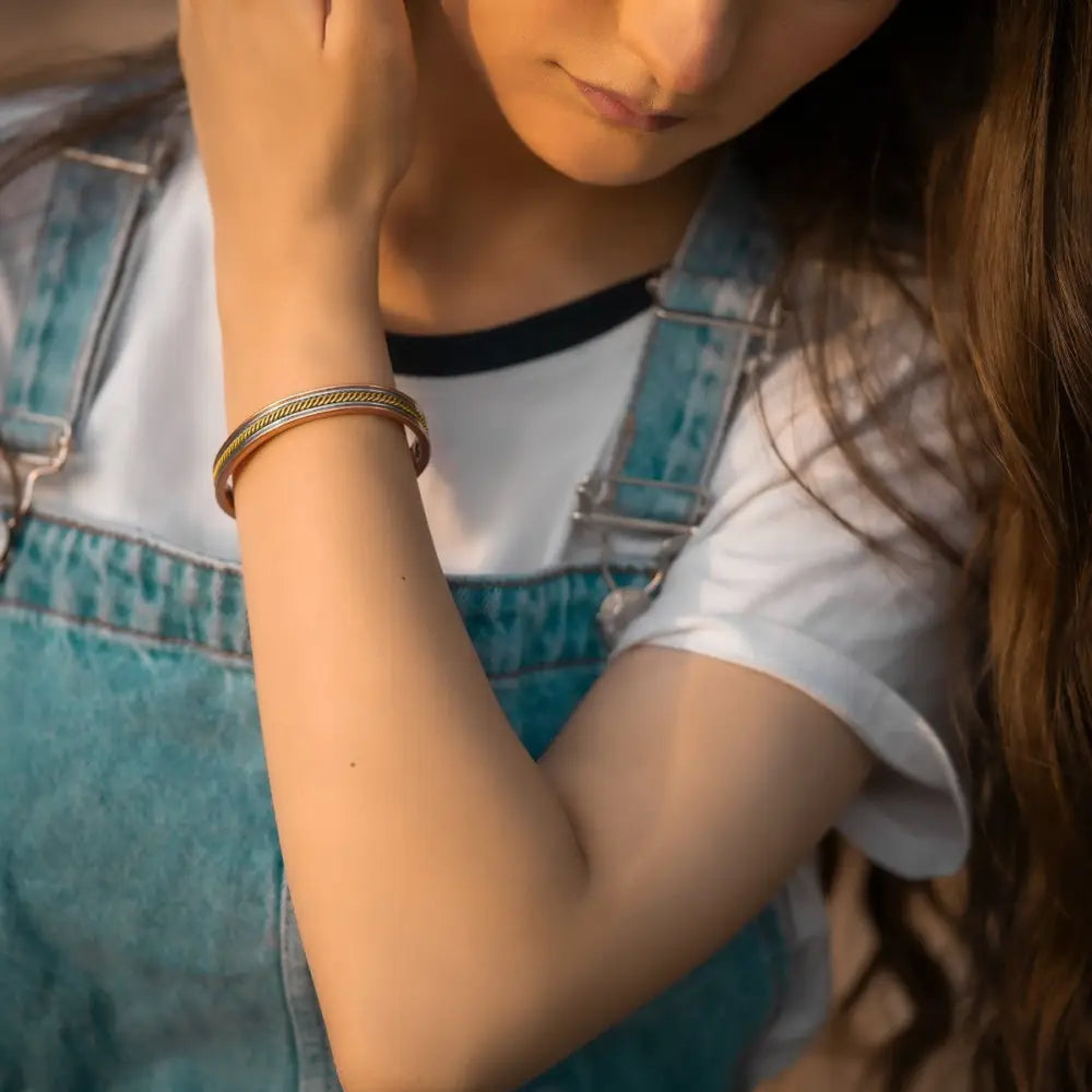 A sleek rose gold twisted copper magnetic therapy bangle with a textured braided metal design worn on the wrist