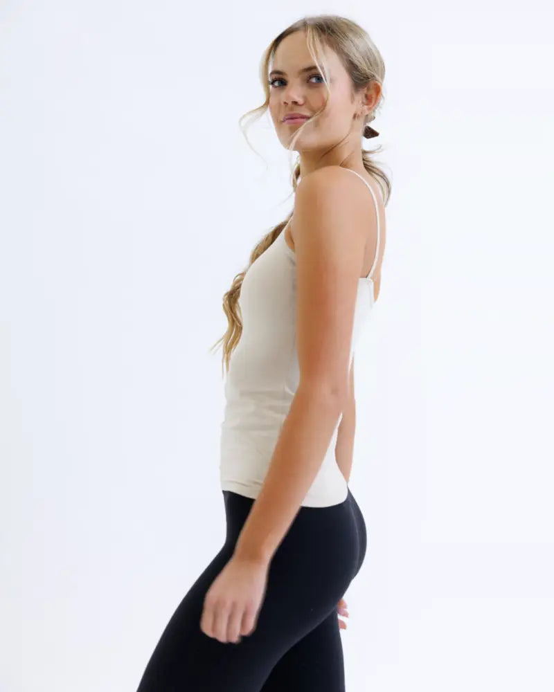 A woman wears a cream-colored wonder cami cotton stretch sleeveless tank top with thin straps and fitted silhouette