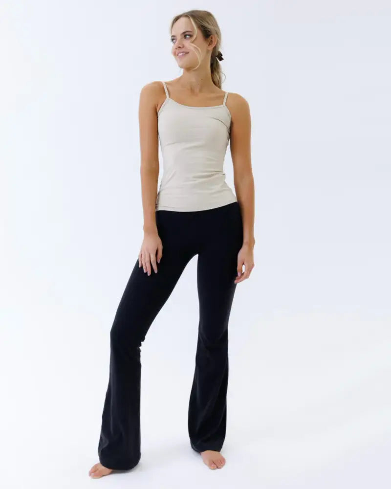 A woman wearing a beige cotton stretch wonder cami layering tank top paired with black flared pants