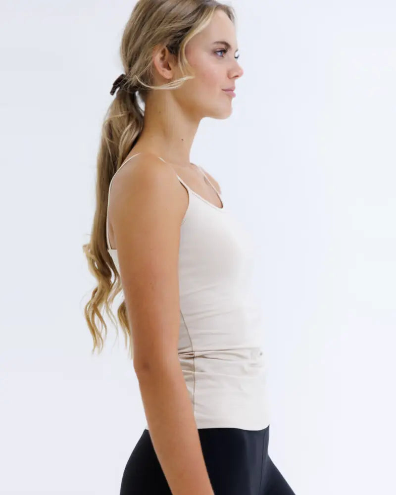 A woman wearing a white wonder cami cotton stretch layering tank top with thin straps and subtle ruching at the waist
