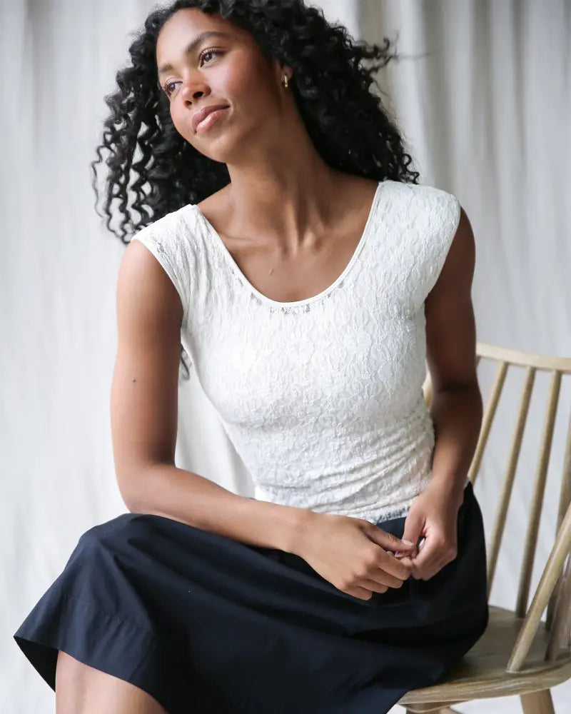 White lace sleeveless top with subtle textured pattern and delicate embellishments along the neckline