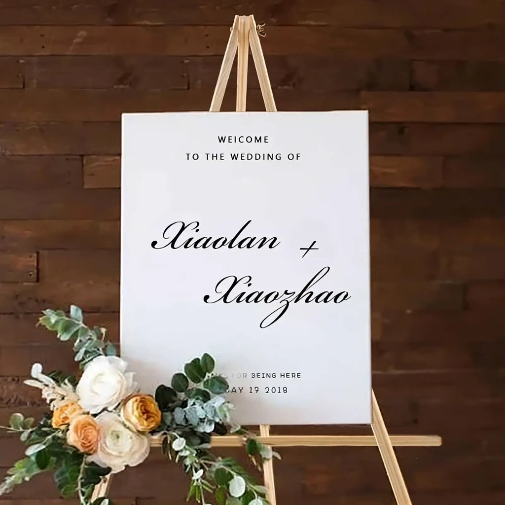 White wedding welcome sign with black cursive script on wood display easel decorated with fresh flowers for weddings