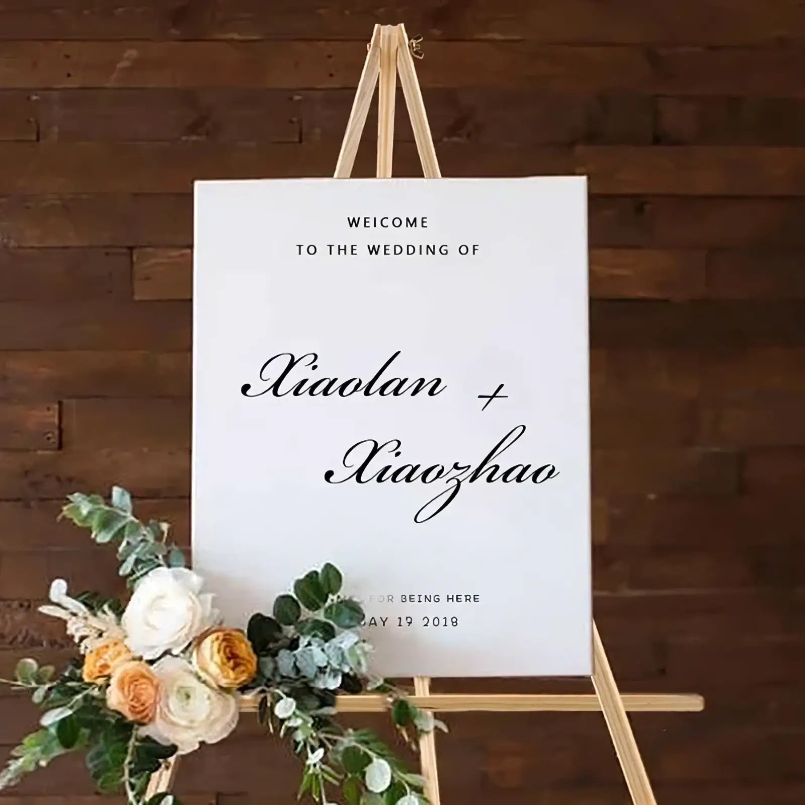 White wedding welcome sign with black cursive script on wood display easel decorated with fresh flowers for weddings