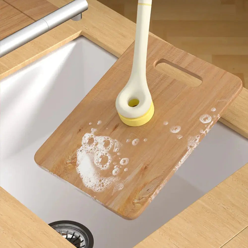 Eco friendly wood pulp kitchen scrub brush with yellow and white rounded head resting on wooden cutting board