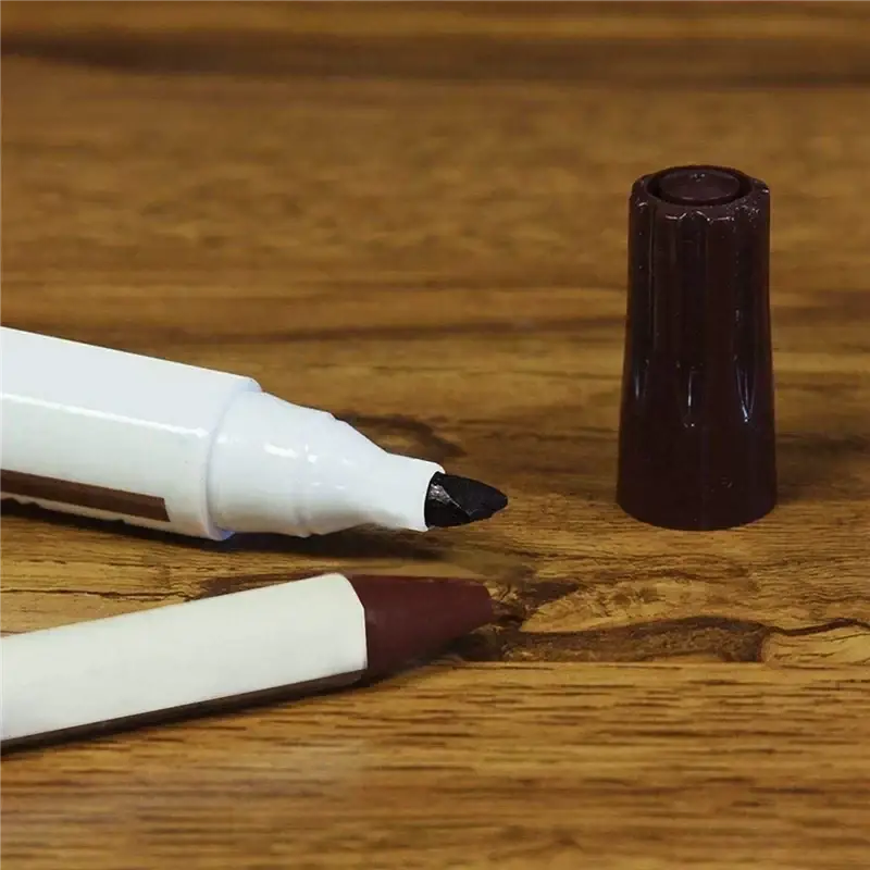 White-bodied wood repair marker with black tip and dark brown cap beside a second marker and wax sticks kit