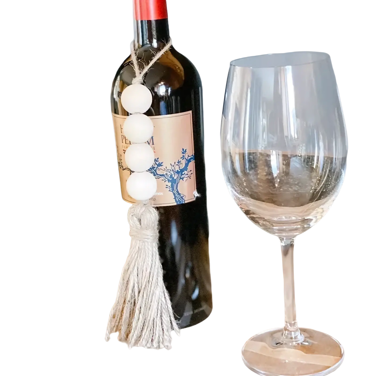 A dark glass wine bottle decorated with a white wooden bead garland and matching tassel ornament