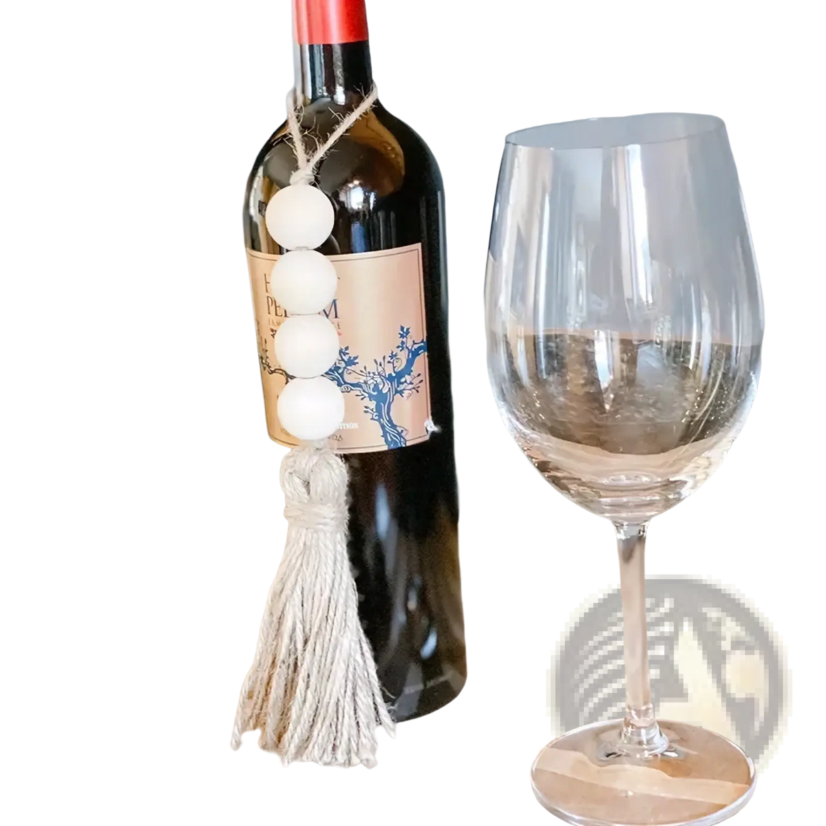 A dark glass wine bottle decorated with a white wooden bead garland and matching tassel ornament