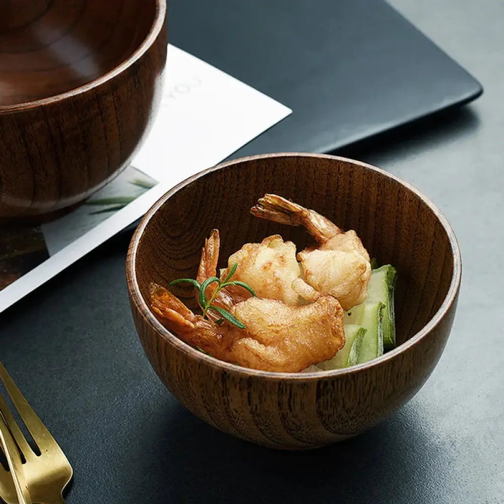 A handcrafted Japanese style natural wooden bowl with warm finish and visible grain holds fried shrimp garnished with rosemary