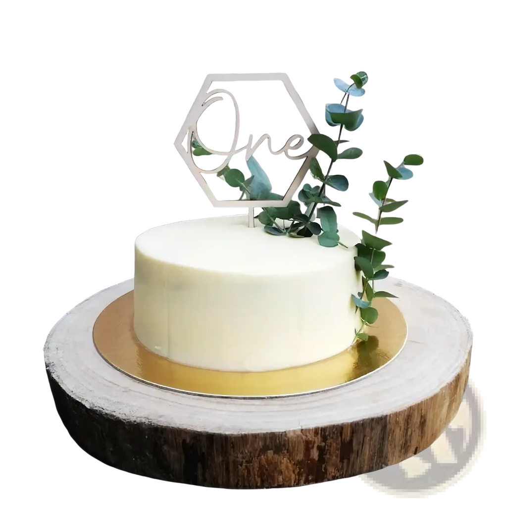 A sleek off-white frosted cake with a wooden hexagonal one cake topper and fresh green eucalyptus sprigs