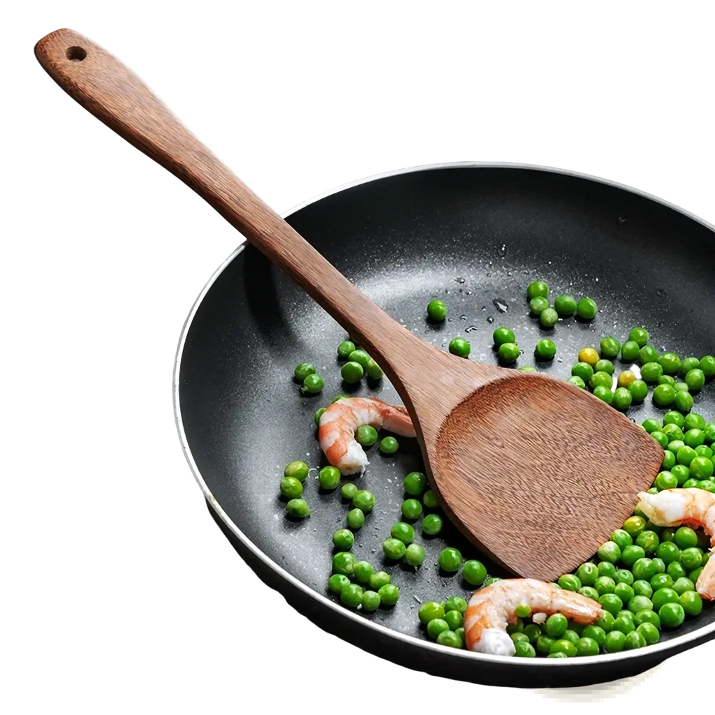 A wooden kitchen spatula with a smooth finish and curved handle resting in a black non-stick frying pan